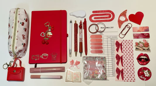 Collection of red stationery items including a notebook, pens, and decorative elements on a white surface.