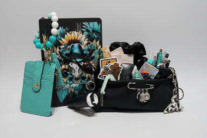 A styled flat-lay of a black canvas organizer pouch filled with stationery and accessories, next to a turquoise leather card holder and a black notebook with a colorful skull graphic, set against a background of white storage drawers filled with colorful pens.