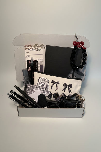 Collection of black stationary items including journal, pencil bag, pens, charms