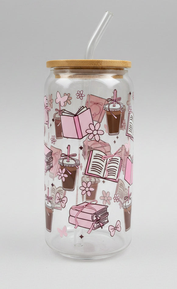  a clear glass tumbler with a bamboo lid, decorated with pink illustrations of books, flowers, and gift boxes, set against a blurred green outdoor background.