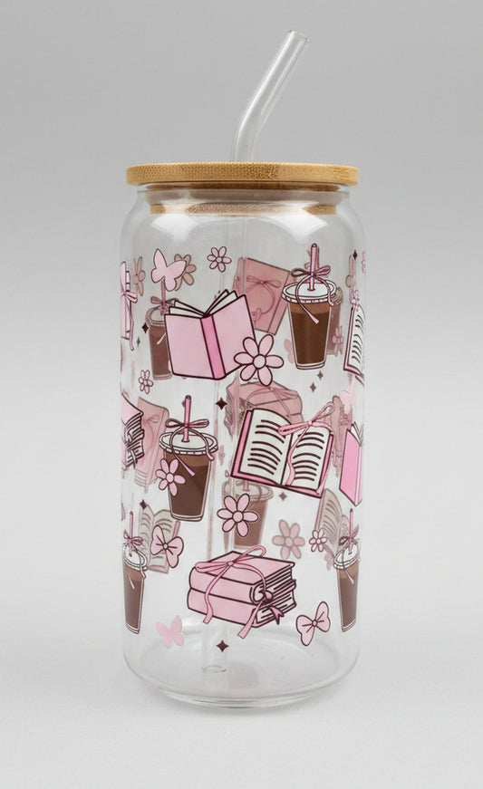  a clear glass tumbler with a bamboo lid, decorated with pink illustrations of books, flowers, and gift boxes, set against a blurred green outdoor background.