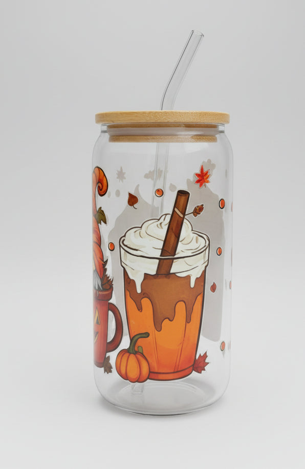 A clear glass tumbler with a bamboo lid and clear straw, decorated with a fall drink illustration featuring orange pumpkin, whipped cream, and autumn leaves, sitting on a gray woven outdoor table.