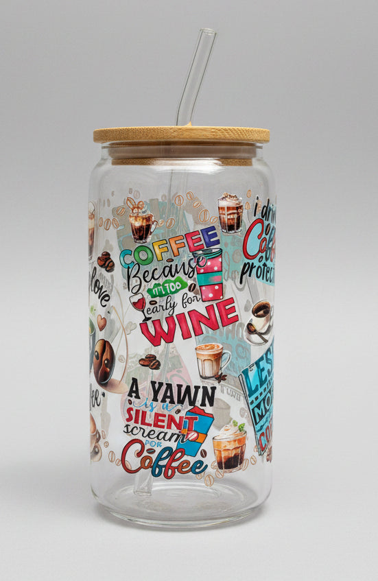 Glass tumbler with colorful coffee-themed text and images on a wooden surface outdoors.
