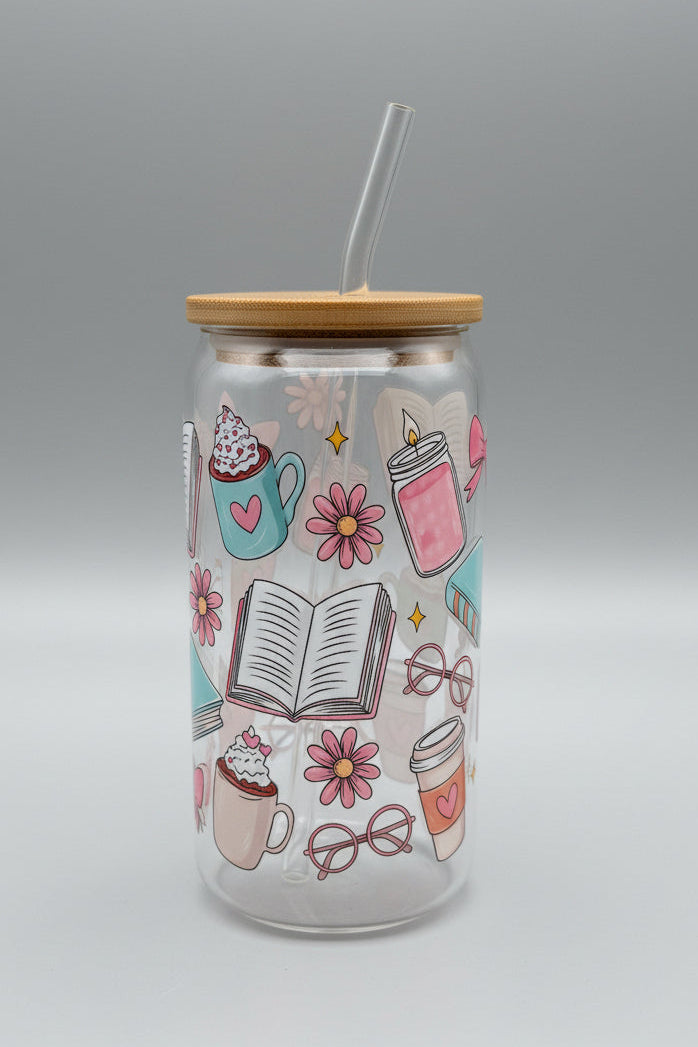 Tall glass jar with a lid and straw, featuring illustrations of coffee cups, books, and flowers on a cardboard background.