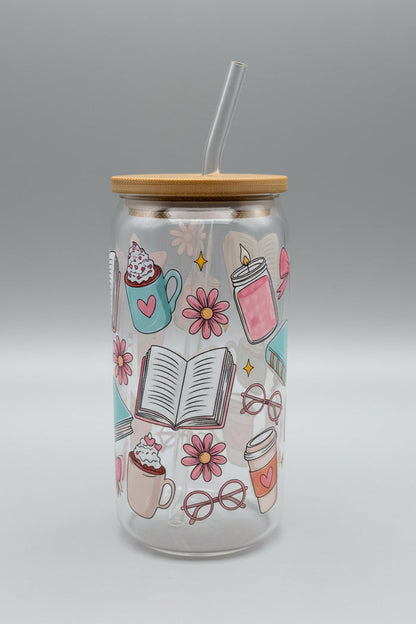 Tall glass jar with a lid and straw, featuring illustrations of coffee cups, books, and flowers on a cardboard background.