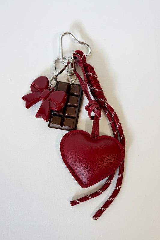 Red heart-shaped keychain with chocolate bar and bow on a white background