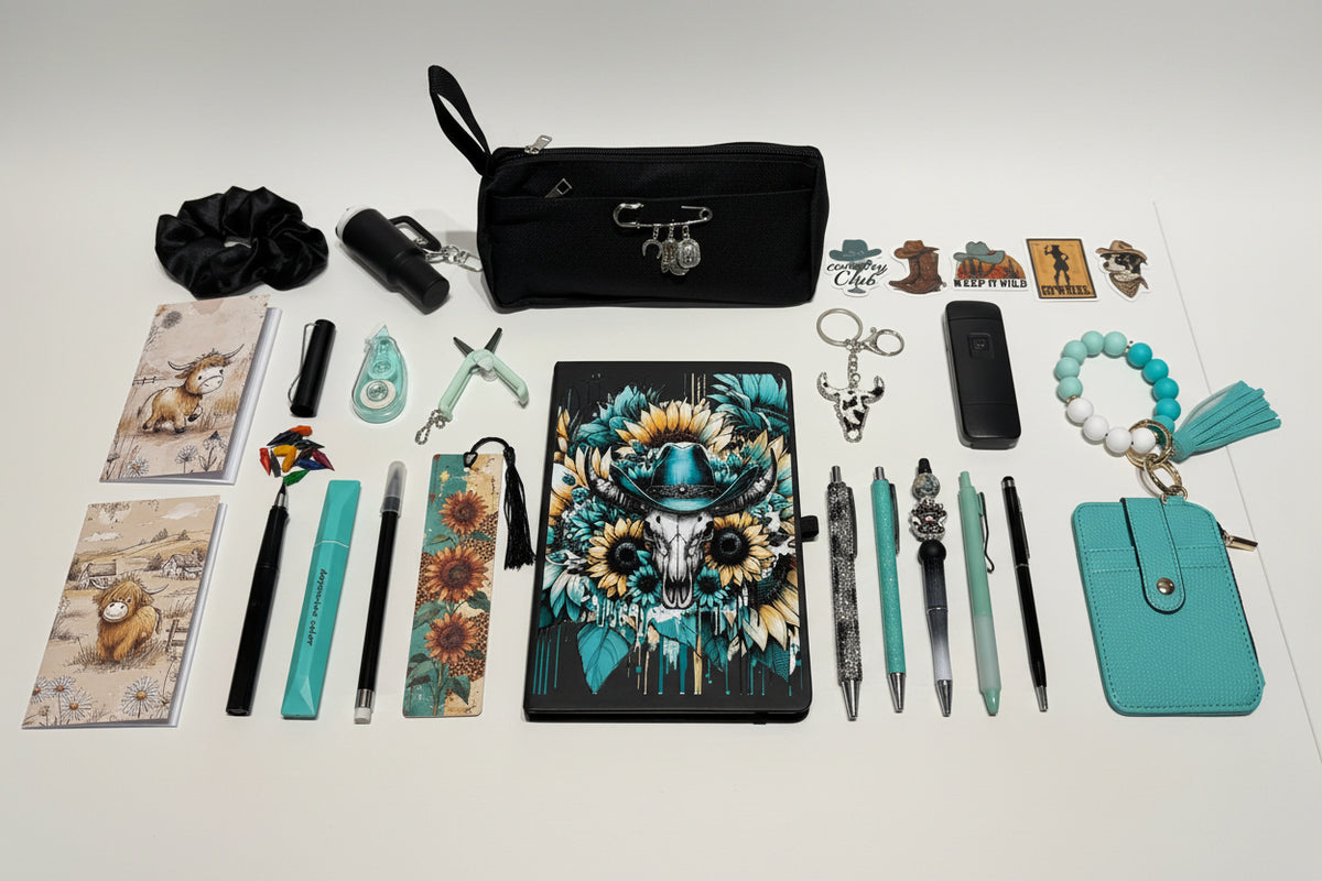 A curated flat-lay of various stationery and lifestyle accessories arranged on a white table in front of a white organizer drawer unit. The central focus is a black tablet case decorated with a colorful skull wearing a sunflower hat.